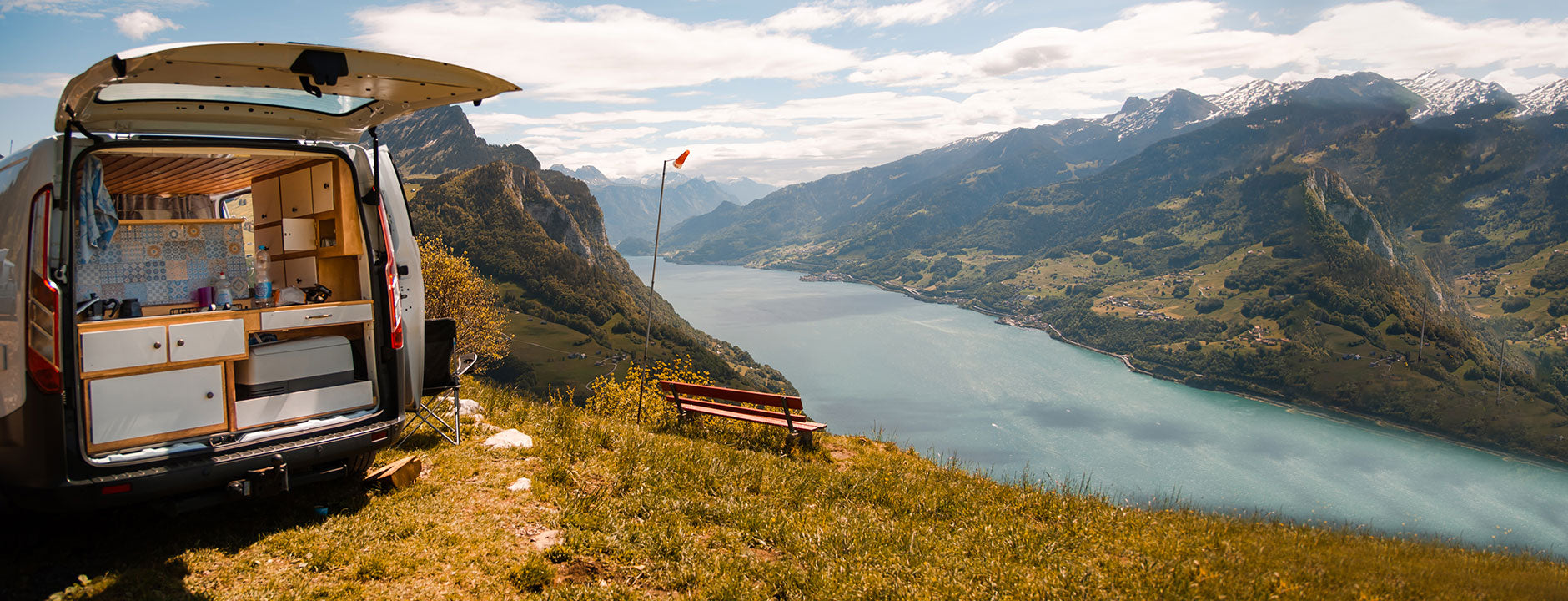 Van parked on a grassy hill with a scenic view of a lake and mountains.