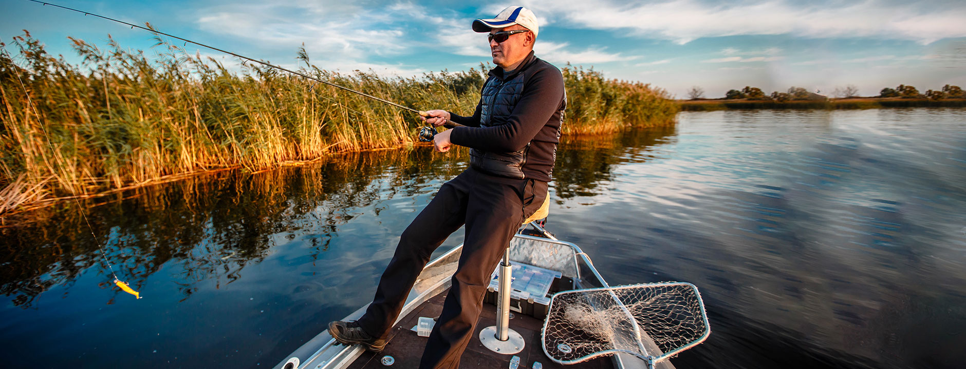 Man fishing on a boat by a lake with reeds in the background