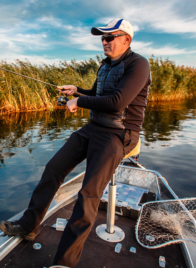 Man fishing on a boat by a lake with reeds in the background
