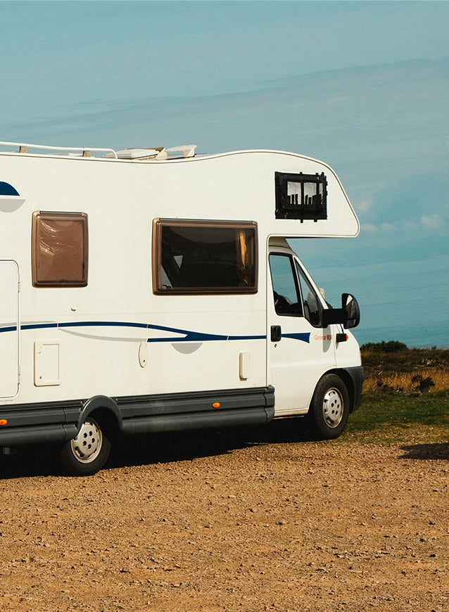 White RV with blue stripe parked on a dirt road under a clear blue sky.